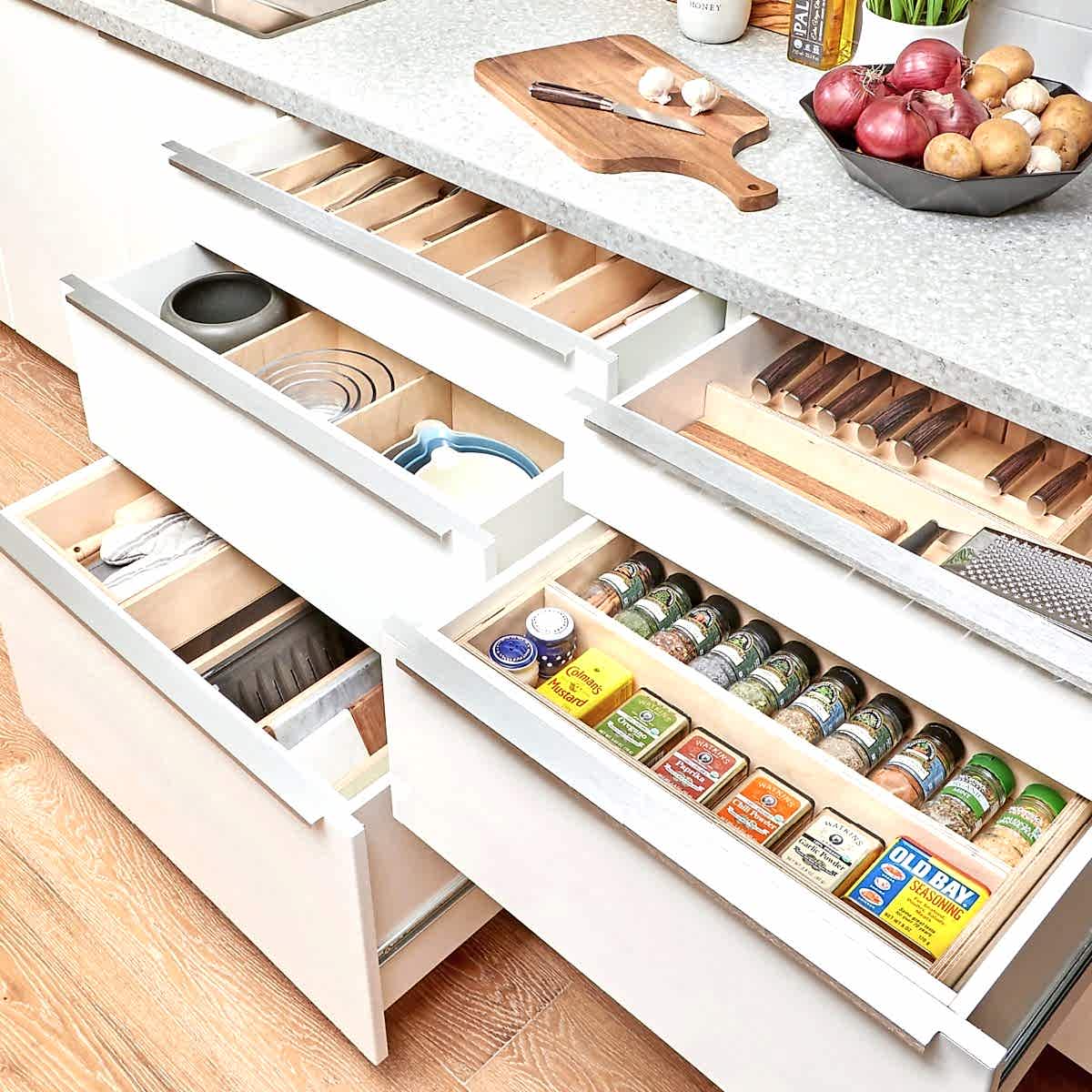 Organized kitchen drawers contain utensils, pots, and spices, revealing efficient storage solutions. The countertop displays garlic, vegetables, and a cutting board, enhancing a cooking environment.