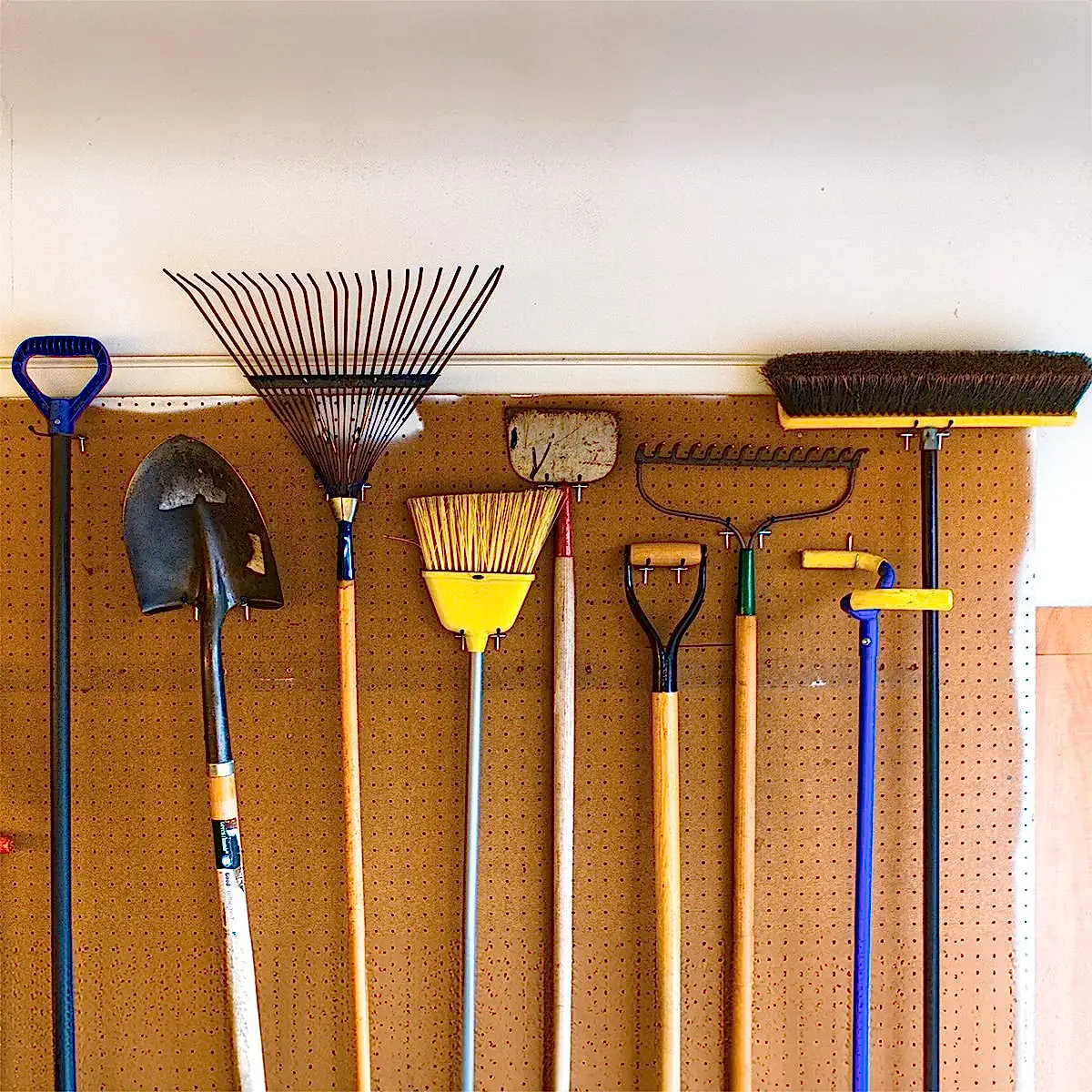 Household and garden tools stored in garage on pegboard wall in an organized and tidy fashion.